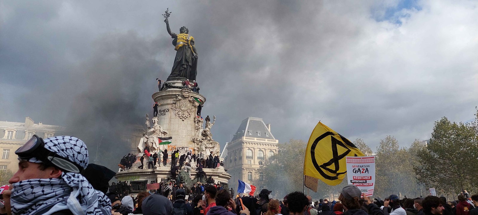 Demonstranten am Denkmal auf dem Place de la République in Paris, umgeben von Rauch und Protestfahnen.